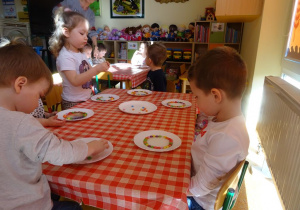 Dwoje dzieci obserwuje jak rozpuszczają się cukierki w wodzie na talerzykach.